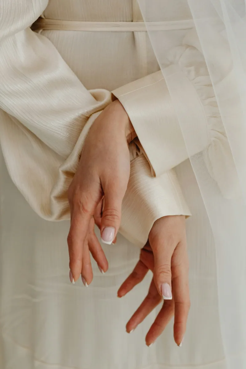 Mains élégantes d’une mariée en robe raffinée, symbole de la touche spéciale des services de coiffure à domicile le jour du mariage