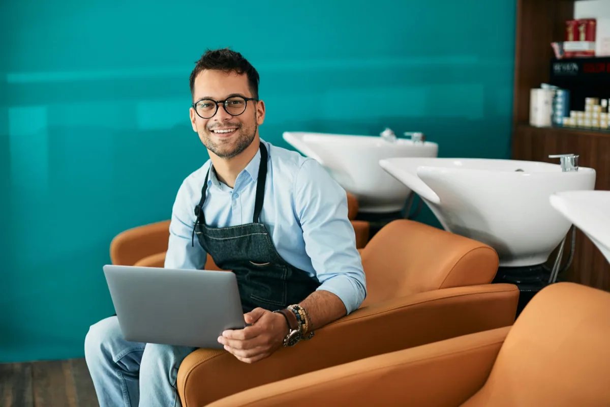 Coiffeuse utilisant un ordinateur portable dans un environnement de salon moderne pour gérer les rendez-vous en ligne et renforcer sa présence digitale